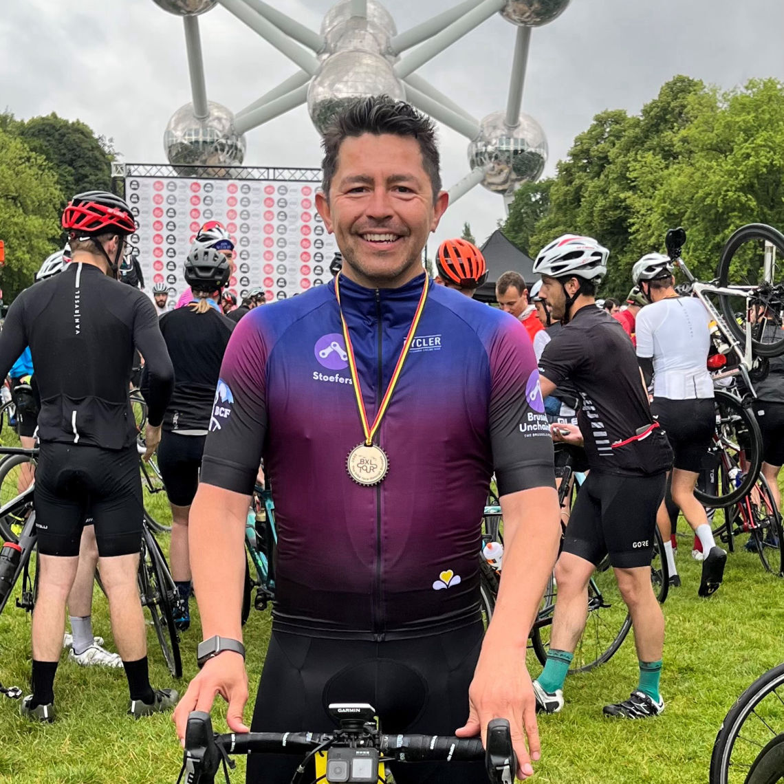 Cyclist Jay standing in front of the Brussels Atomium wearing our team kit