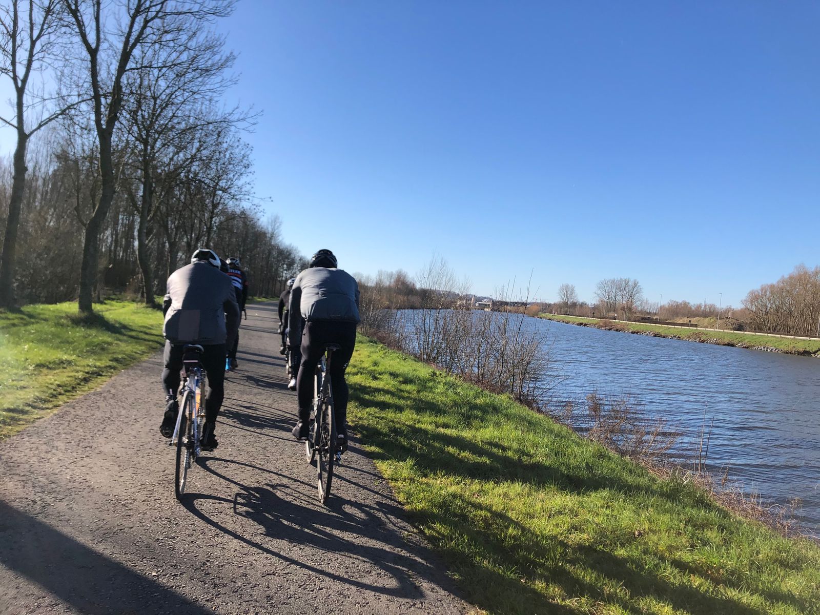 Cyclists in a 2x2 formation riding next to canal near Ghent